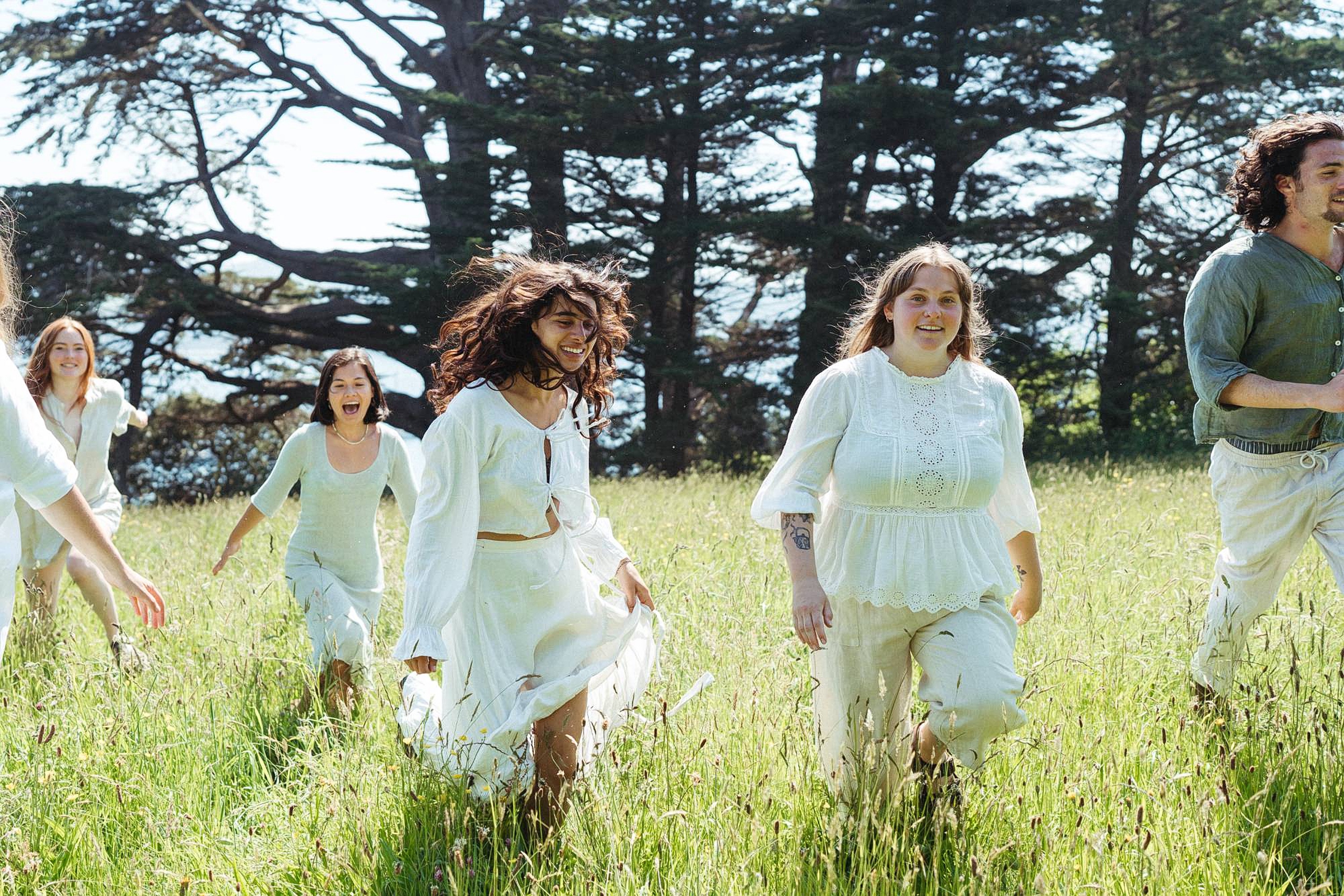 Friends in white running through long meadow grass